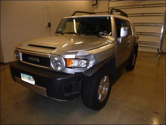 Front view of crash SUV showing damage to left fender near turn signal assembly.